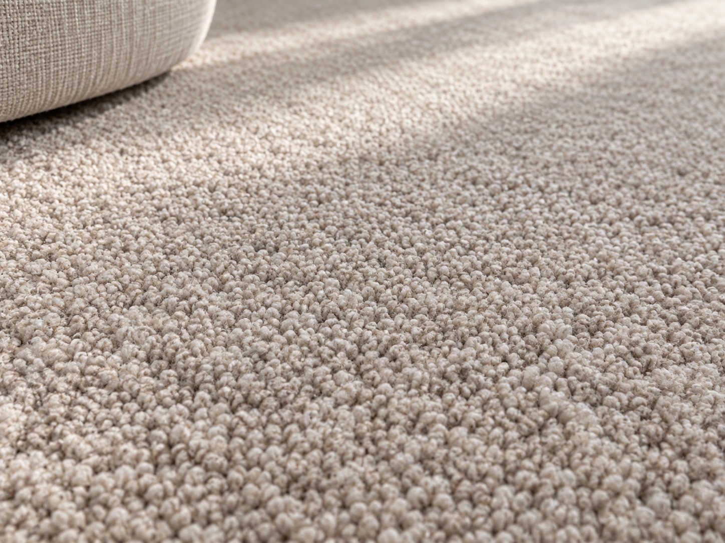 A close-up of a light beige carpet showing the individual twisted yarn tufts that make up the pile